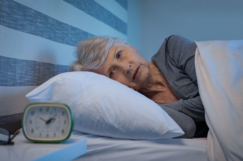 Starsza kobieta lezy w łóżku i nie może zasnąc przez częste oddawanie moczu