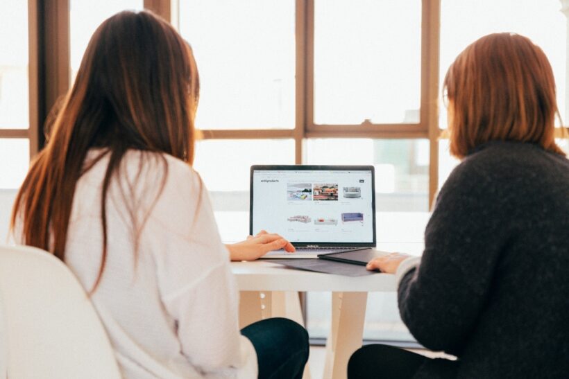 dwie kobiety studiujące wzornictwo siedza przy biurku na przeciwko laptopa